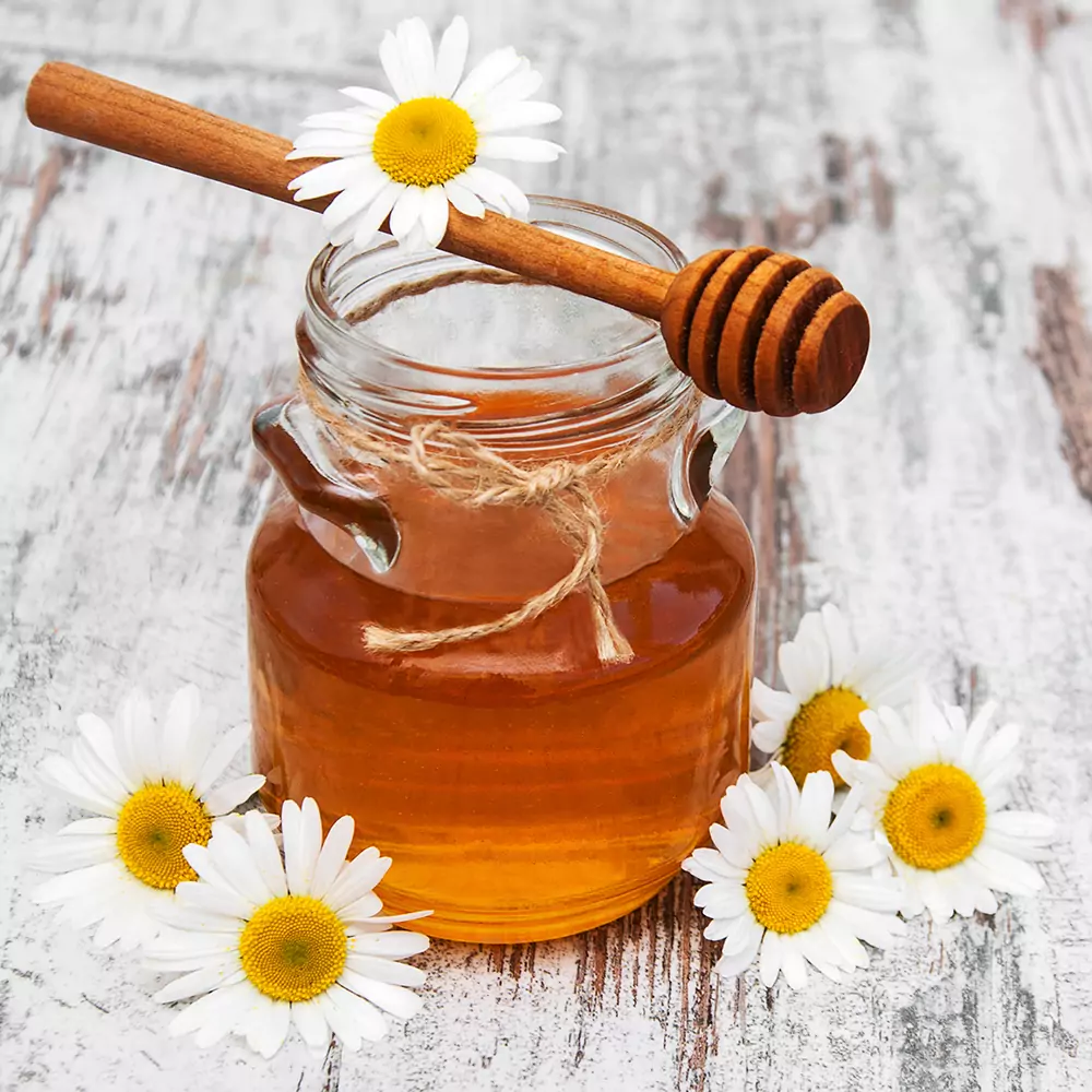 Kategorie Honig - Zu sehen ist ein Honigglas und Blüten auf einem Tisch